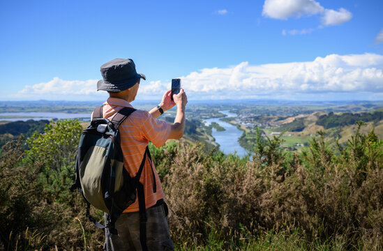 Man taking photos using smartphone of Huntly and Waikato River. Hakarimata Summit Track. Waikato. New Zealand.