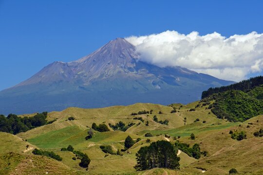 spectacular view of mount taranaki and fanthams peak in egmont national park across rolling farmlands on a  sunny day near te wera on the forgotten world highway on new zealand's north island 