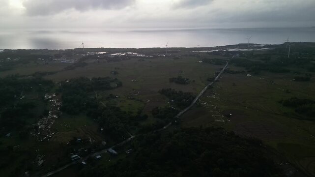Sweeping view of wind turbines dotting the landscape of Guimaras Island, Philippines, with farmland and distant ocean. Ideal for renewable energy or travel content.