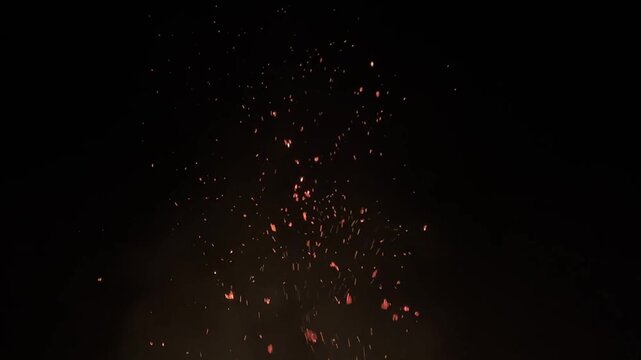 An artistic shot of glowing embers from a large fire floating up into the cold night sky.