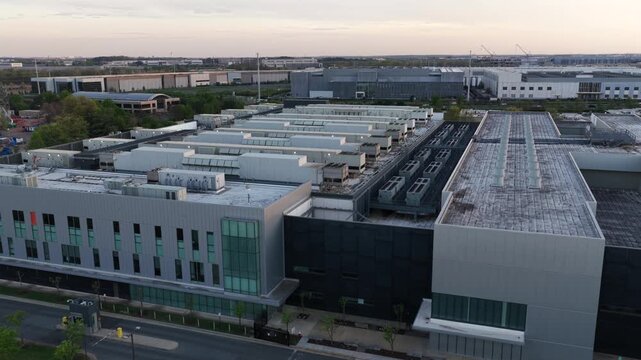 New developed modern data center in Ashburn, Virginia at sunset with rooftop HVAC cooling systems, large scale infrastructure and surrounding tech corridor buildings in Data Center Alley. Aerial wide