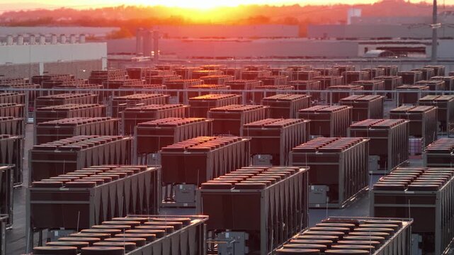 Aerial sunset view of data center in Ashburn, Virginia with rows of industrial cooling units and rooftop HVAC systems glowing in warm light across large scale server farm infrastructure. Wide shot.