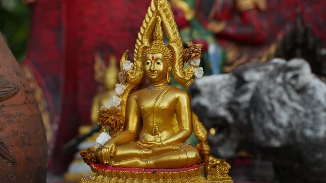 Golden Thai Buddha Statue with Flame Halo Seated on Ornate Base with Candle Flame and Red Offerings