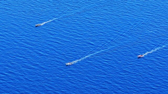 Three boats move in parallel, leaving trails on the expansive blue ocean, showcasing maritime activity.