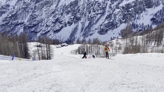 Group of skiers descending a groomed slope in the Alps with majestic snow-capped mountains in the background. Winter sports activity on a sunny day at a ski resort with breathtaking mountain panorama.