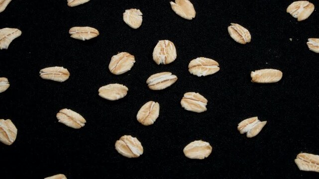 Extreme macro of scattered organic rolled oat grains on black background rotating.