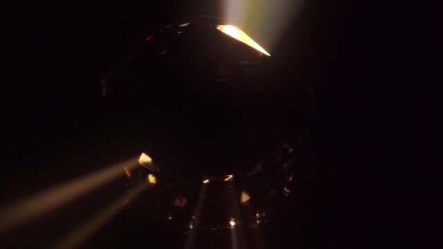 Abstract dark crystal sphere rotating with golden light rays and glowing bokeh flares seamless loop
