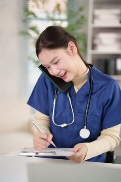 Female healthcare professional multitasking, talking on mobile phone, smiling while writing patient notes, managing medical tasks in a healthcare office, busy nurse communication