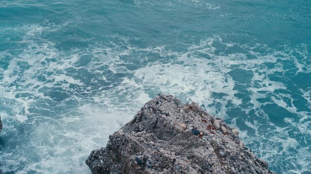 Blue ocean waves surrounding a textured rocky formation during blue hour, creating a moody coastal scene with contrast between solid rock and moving water.