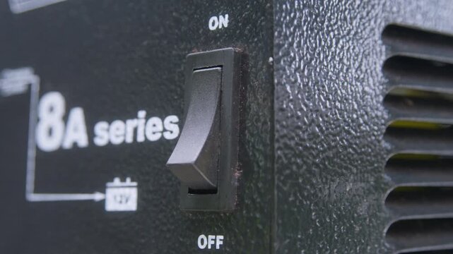 Close up activation of 12v battery charger On Off toggle switch. Activation both ways. Maintenance, power management and electrical charging concept