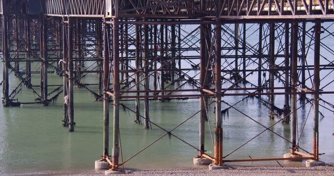 Wide shot looking down and through the rusted metal support frame for Brighton Palace Pier