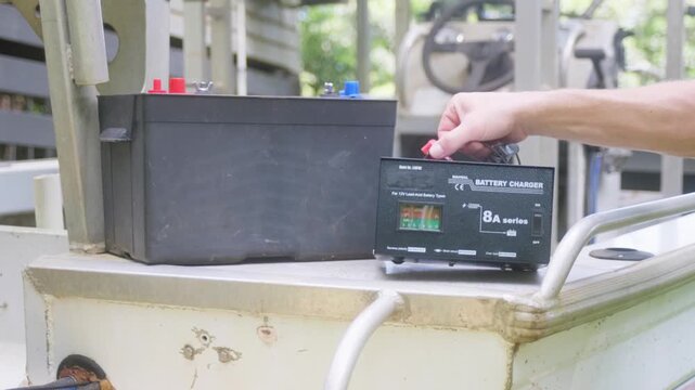 Man connecting a 12V battery charger to a marine battery in a small aluminium boat. Boating maintenance, power management and electrical charging concept. Clip 5
