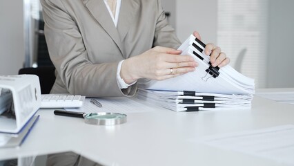 Businesswoman hands organizing stack of papers with binder clips, working on financial documents...