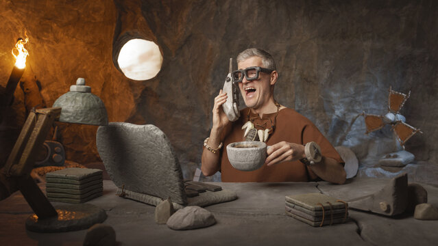 Business in the stone age: office worker having a phone call and drinking coffee