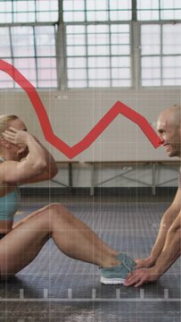 Vertical video: Woman doing sit-ups in gym while man anchoring shoes, gym telemetry tracking effort