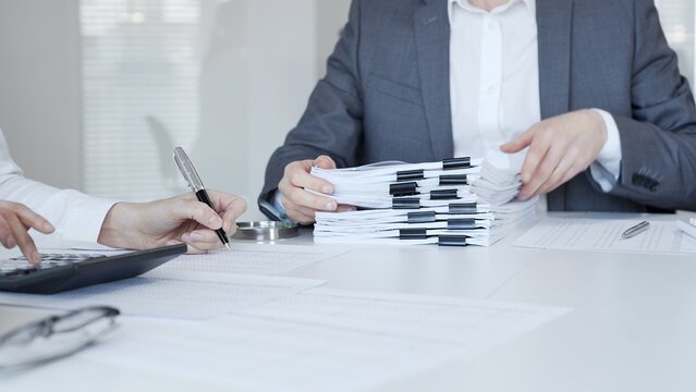 Business people reviewing financial documents, calculating tax, auditing corporate accounting records, and processing paperwork in office. Audit and taxes in business