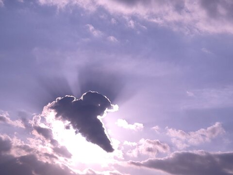 Dramatic sun rays breaking through dark cloud with silver lining effect in purple twilight sky
