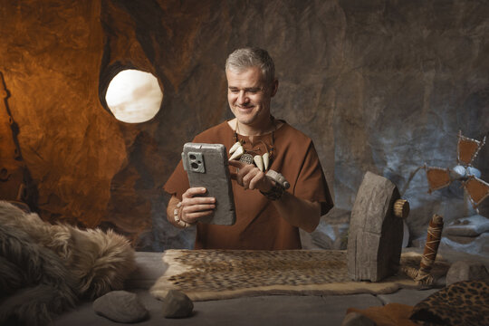 Prehistoric man using his smartphone while ironing at home
