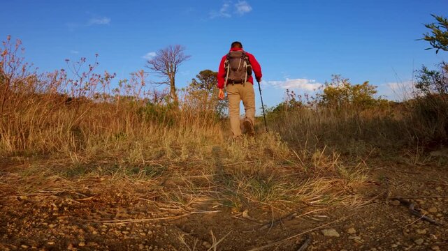 Man with backpack and poles hiking away on a dirt path with la malinche volcano in the background