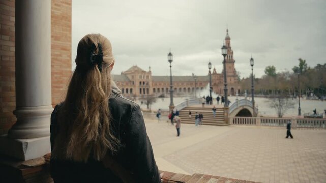 Female tourist seen from behind looking out over Plaza de Espana in Seville, Spain, capturing travel perspective, iconic architecture, and a calm moment of observation.