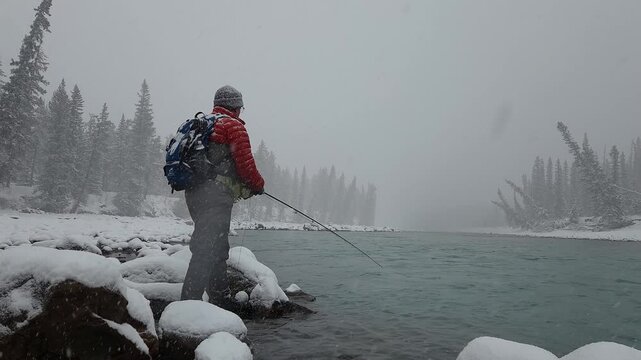 Fly fishing angler casting and stripping line in snowstorm along glacial river, with snow accumulating on gear, capturing action, endurance, and winter outdoor adventure.