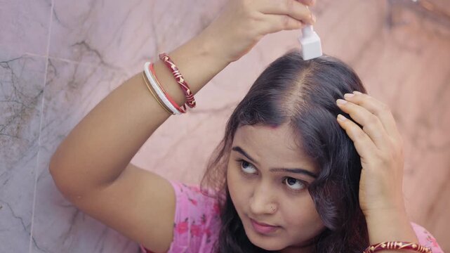Microneedling treatment, androgenic alopecia, hair loss. Indian woman using derma stamp on thinning scalp area in the modern bathroom.