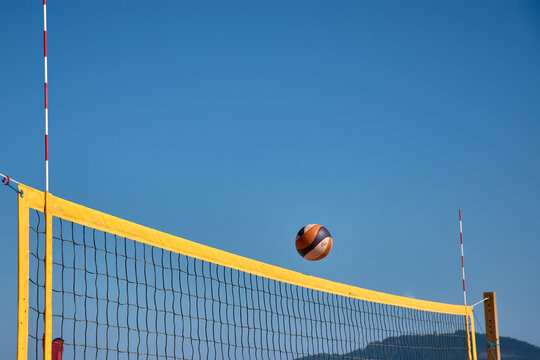 Volleyball in the air over a yellow net during a beach match in Baiona under a clear blue sky