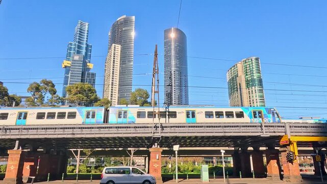Passenger train crossing bridge with skyscrapers in background at Melbourne city center.