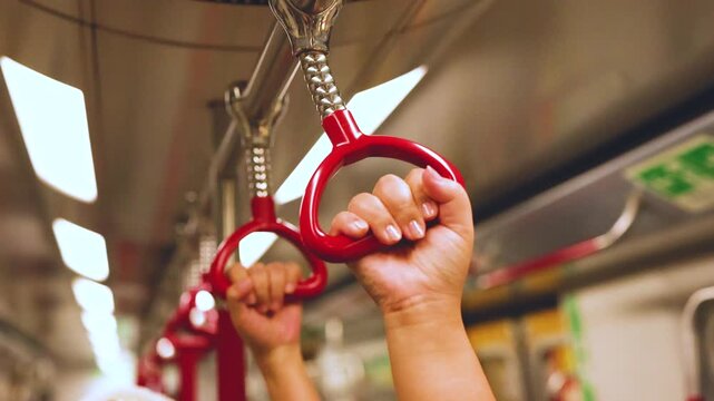 Close up of person's hands gripping red handrails inside moving subway train.