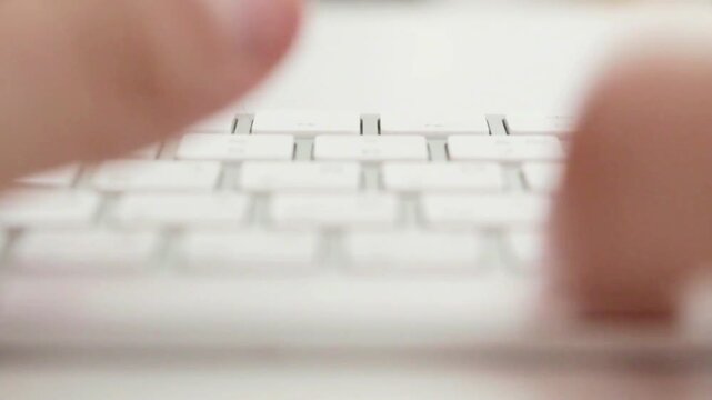 Close-up of a person typing on a white wireless computer keyboard in a bright office environment.

