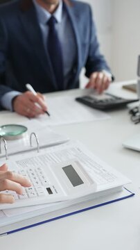Close up of female financial analysts examining documents with male colleague, using calculator at workplace in office. Audit and taxes