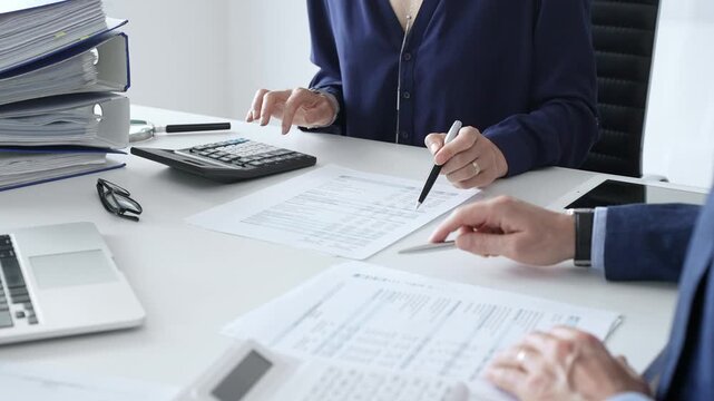 Female financial analysts examining documents, using magnifying glass and calculator while discussing corporate data with a male colleague. Audit and taxes in business