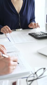 Female financial analysts with male colleague examining documents, using magnifying glass and calculator while examining corporate data at workplace in office. Audit and taxes in business