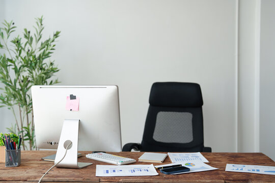 Modern empty office desk featuring a computer monitor, keyboard, and business documents, with an ergonomic chair and potted plant enhancing the workspace environment