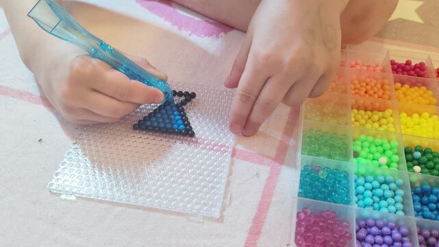 Young hands placing colorful water beads on template using pipette. Kids craft activity with aqua mosaic beads for creative play and art project.