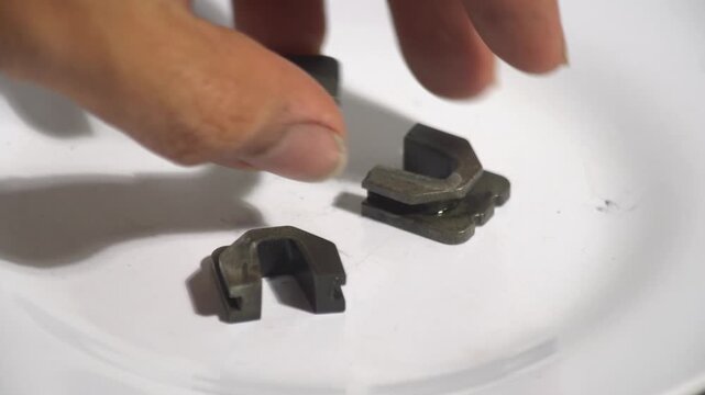 Close up of small industrial metal U-shaped clips or fasteners on a white plate. A hand enters the frame to pick up the mechanical components. Concept of hardware assembly, spare parts inventory, and 