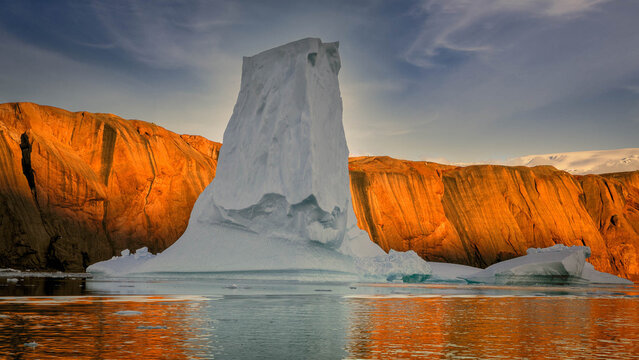 The huge iceberg on the colorful sunset sky background. Breathtaking magic Antarctic landscape. The ice and snow covered glacier floating among the frozen polar ocean. Overwhelming fairy tale scene.