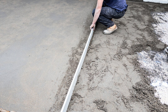 Worker leveling concrete with screed for slab foundation