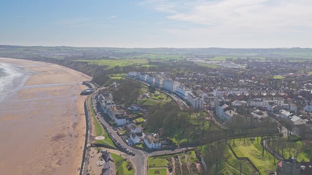 The Crescent and Royal Crescent in Filey North Yorkshire England above Ravine Road and Filey Promenade overlooking Filey Bay sandy beach and North Sea with inland farmland, drone ascent shot