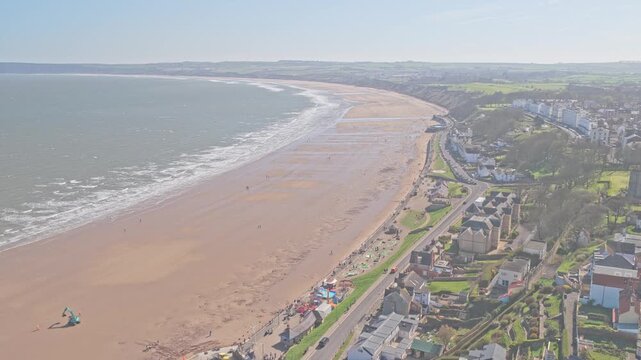 Filey Bay coastline along Ravine Road Filey North Yorkshire England with wide sandy beach, North Sea waves, promenade and residential strip within curved embayed coastal system, drone ascent