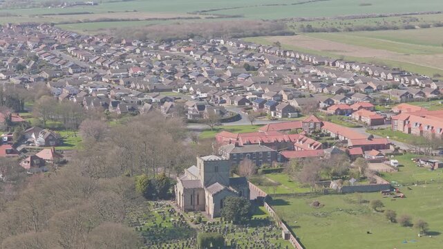 St Oswald Church and churchyard on Church Hill near Ravine Road Filey North Yorkshire England with surrounding suburban housing estate and coastal plain landscape under clear weather, drone view