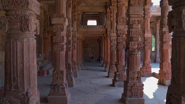 A static shot inside a colonnade at the Qutb Minar complex, featuring rows of intricately carved red sandstone pillars with traditional motifs and architectural details.