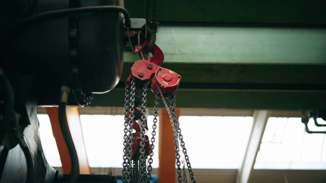 Close-up of a chain hoist system with moving chains lifting heavy loads in an industrial environment.