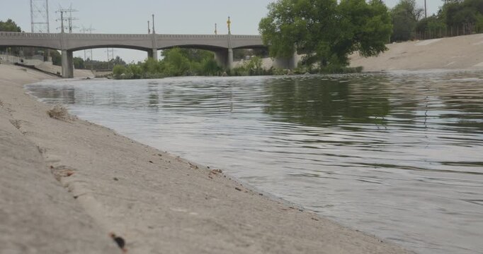 Cinematic daytime 4K 10-bit wide shot captured from the riverbank of the Los Angeles River looking downstream toward a bridge as the river flows through the channel.