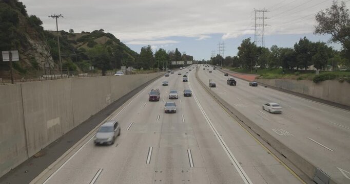 Cinematic daytime 4K 10-bit footage captured from a bridge overpass above a Los Angeles freeway, showing vehicles driving beneath the bridge and heading toward the camera position.