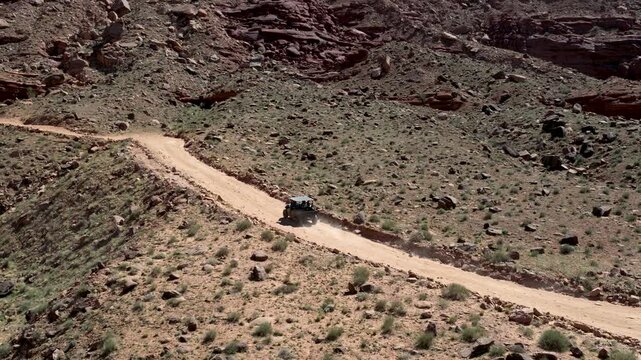 off road adventure with Utility terrain vehicle moves along dusty dirt trail cutting through arid terrain with desert biome along Chicken Corners trail near Moab in Grand County Utah, zoom out reveal