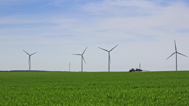 Agricultural machinery spraying field of wheat and wind generators located near the village of Suvorovo, Varna, Bulgaria