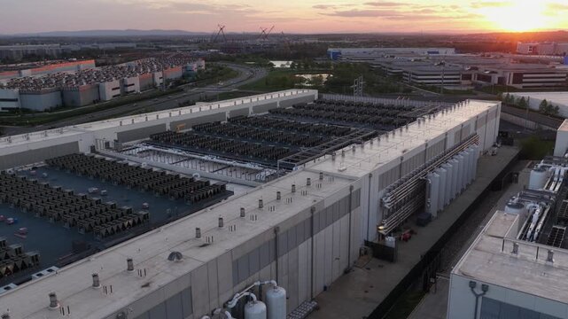 Large-scale data center complex in Ashburn, Sterling, Virginia at sunset with rooftop cooling systems, industrial infrastructure and high-tech cloud computing facilities. Traffic on road. Aerial view.