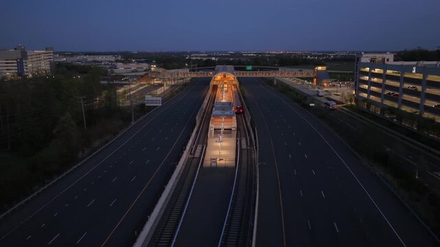 Aerial night flyover of metro station in Ashburn, Virginia with cars driving along highway and illuminated transit platform showing urban transportation infrastructure in Northern Virginia, USA