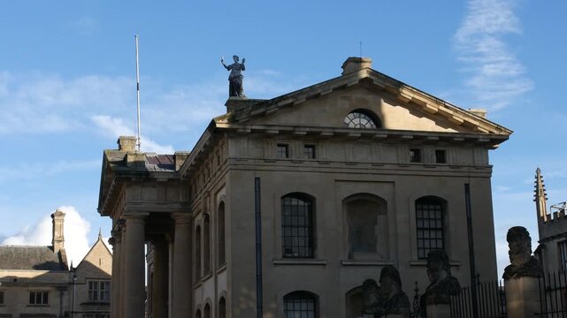 Building at Oxford University with classical pediment and rooftop statue Sheldonian Theatre exterior captured in wide angle under blue sky with historic architecture detail